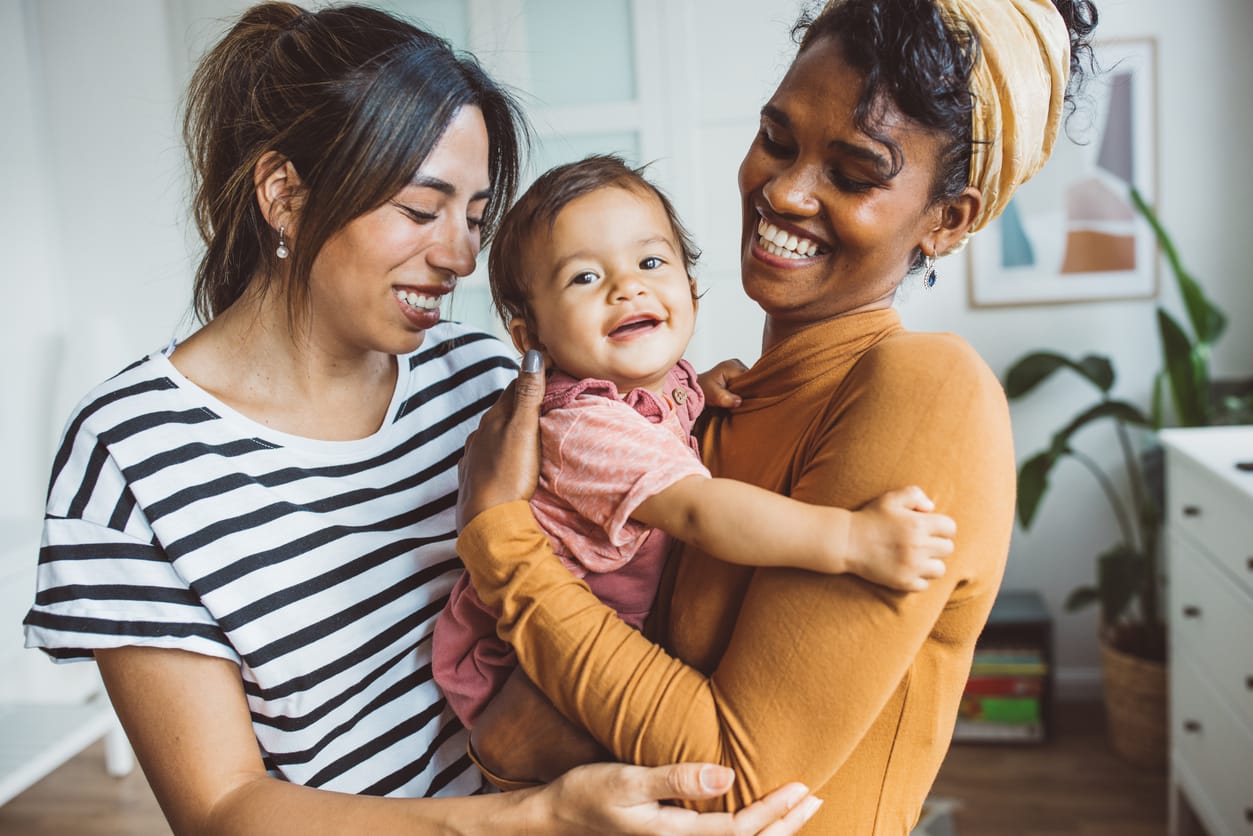 Gay couple with baby at home Young mothers playing with baby girl in living room.